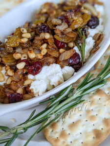A serving dish of Raisin Pine Nut Goat Cheese Appetizer with crackers for dipping.
