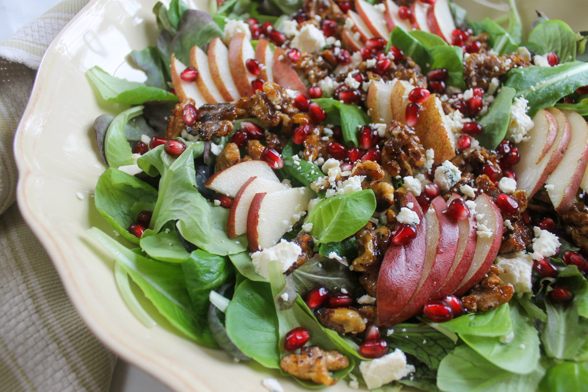A side view of salad greens topped with pear slices, blue cheese and red pomegranate seeds.