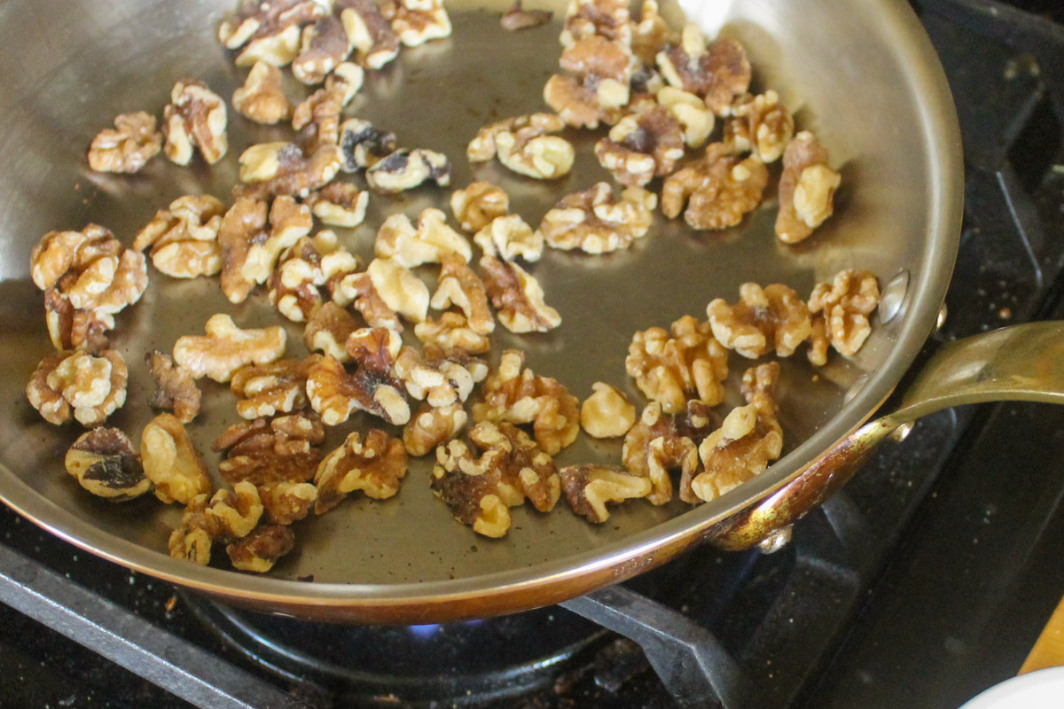 Toasting raw walnuts in a skillet before glazing with honey.