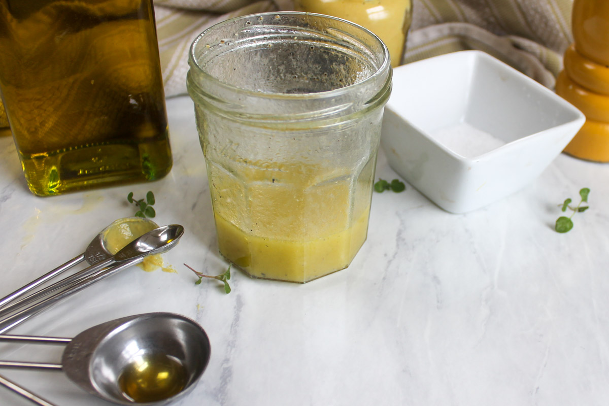 Making the Honey Dressing in a jar next to measuring spoons and a salt dish.