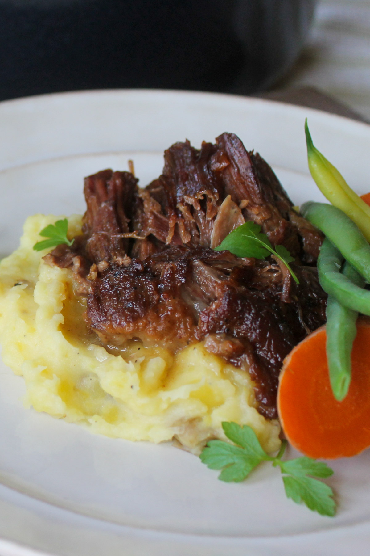 Tender braised beef roast on mashed potatoes with vegetables.