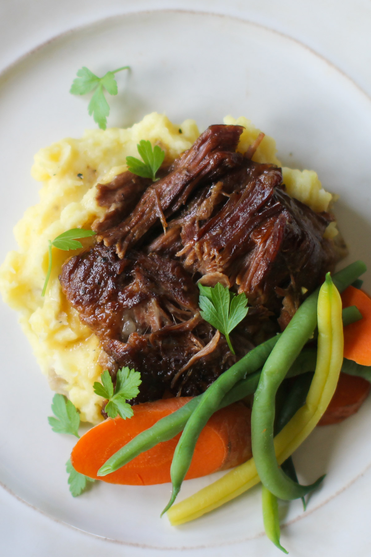 A plate of braised beef roast with mashed potatoes and vegetable sides.