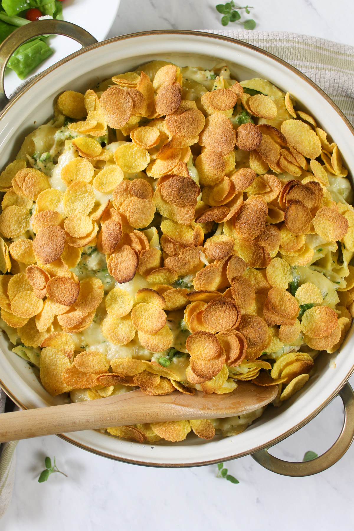 Tuna Broccoli Pasta Bake casserole in a gold rimmed baking dish with cornflake topping.