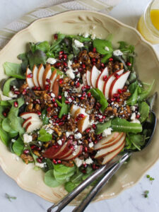 A serving dish of Pear and Blue Cheese Salad with Glazed Honey Walnuts and serving spoons.