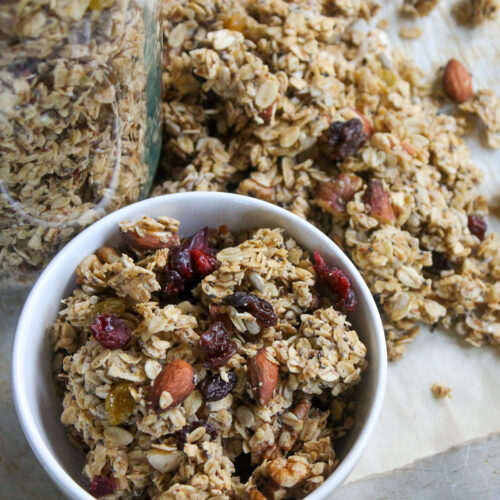 A sheet pan of homemade granola with a bowl and a jar of granola.