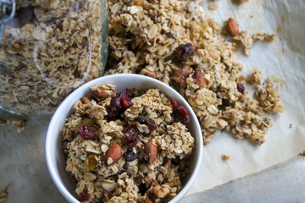 Almond Spiced Granola in a white bowl in front of a jar of granola on a sheet pan.