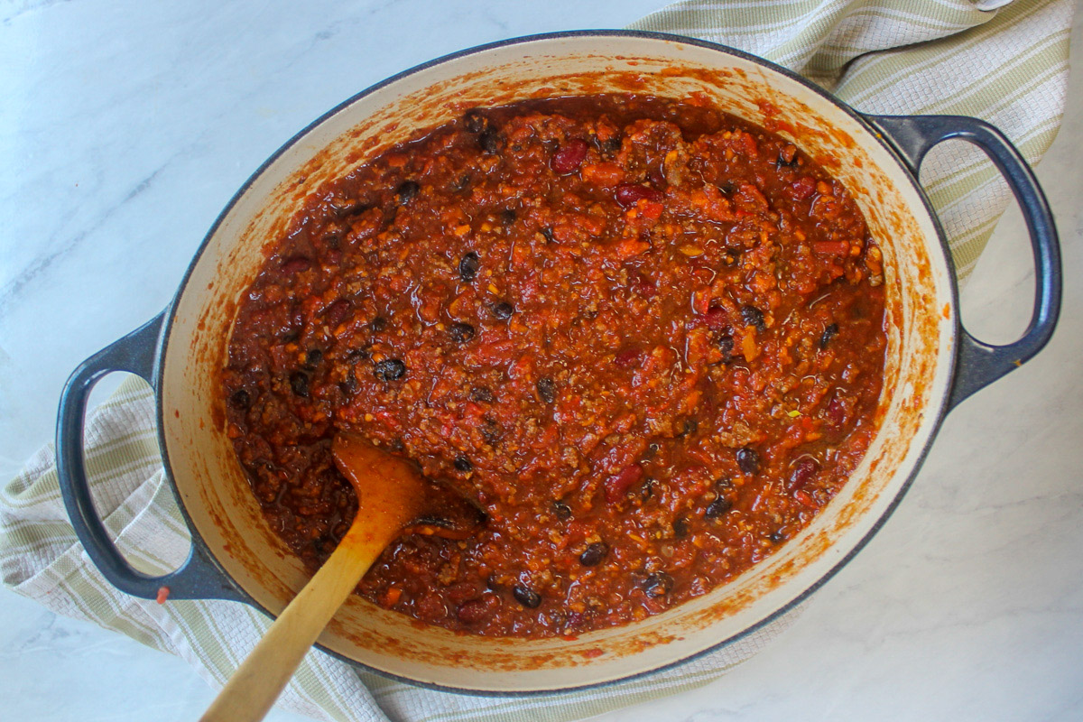 A top down look at the pot of chili as it is finishing with a wooden spoon.