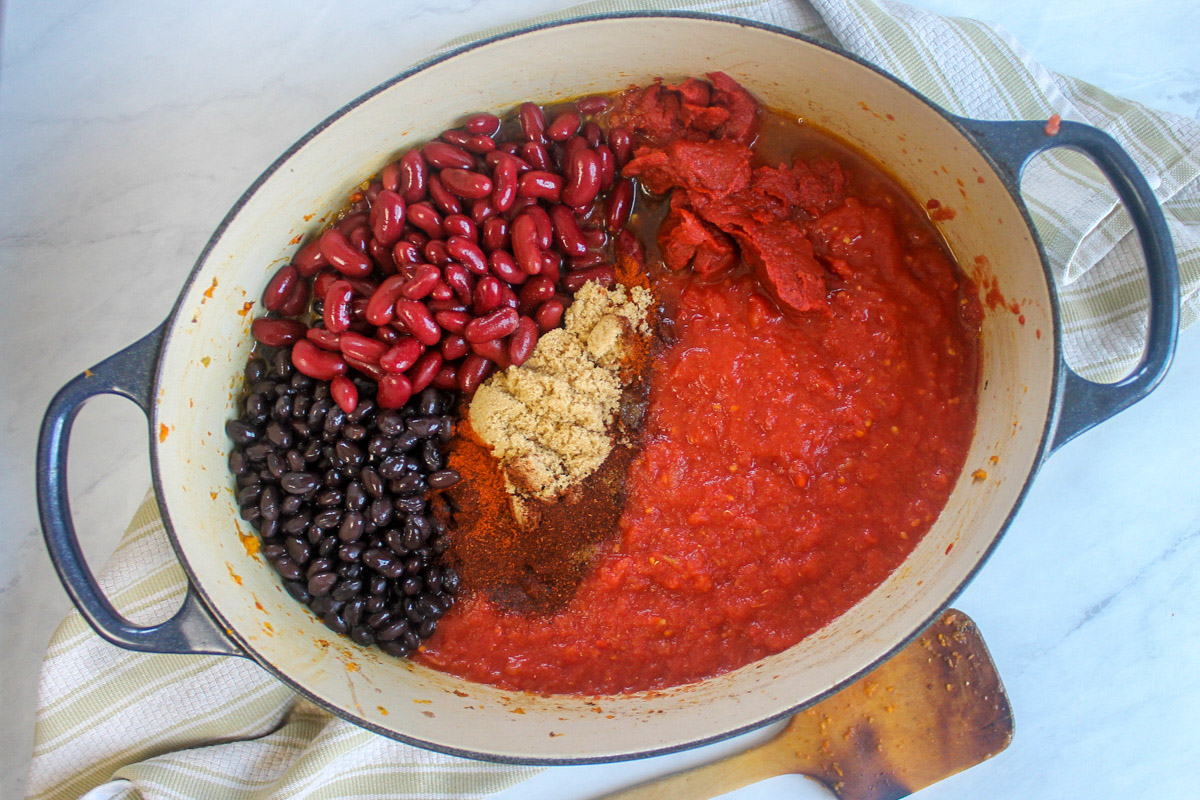 Adding the beans and tomato to a pot of chili to simmer.