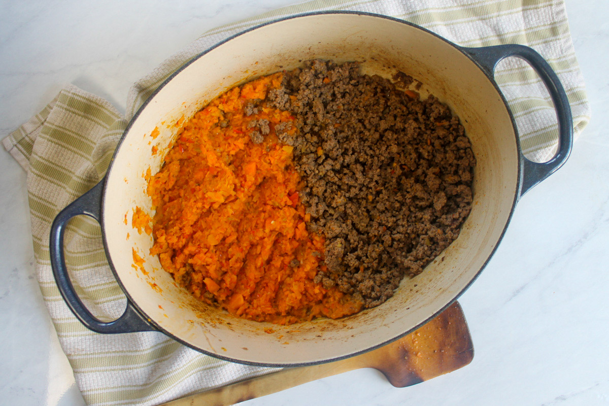 A soup pot with half browning ground beef and half ground of veggies sautéing.