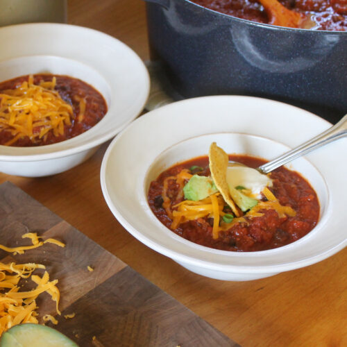 Bowls of chili with toppings in front of the pot of chili.