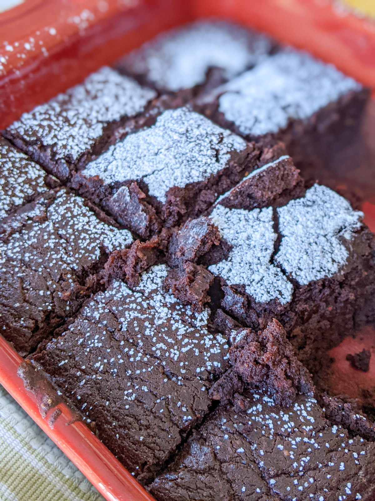 A pan of black bean brownies cut into squares and topped with sifted powdered sugar.