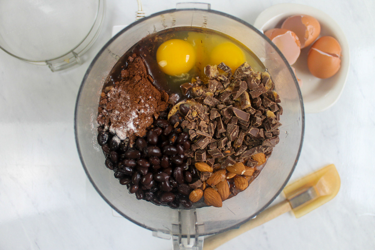 Ingredients for black bean protein brownies added to the bowl of a food processor.