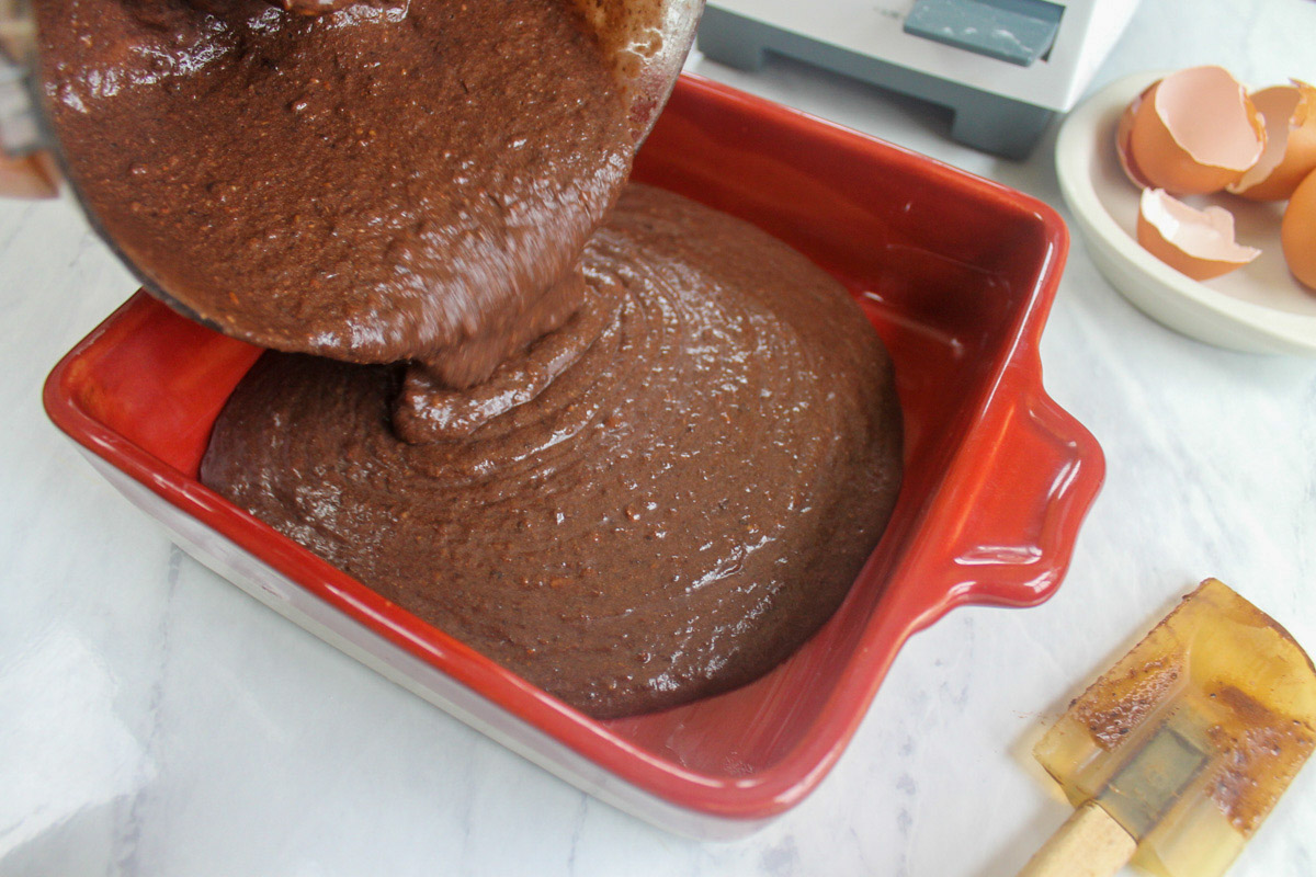Pouring brownie batter from the food processor to a baking dish.