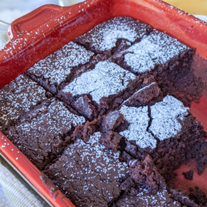 A red baking pan of black bean brownies cut into squares with a white dusting of powdered sugar.