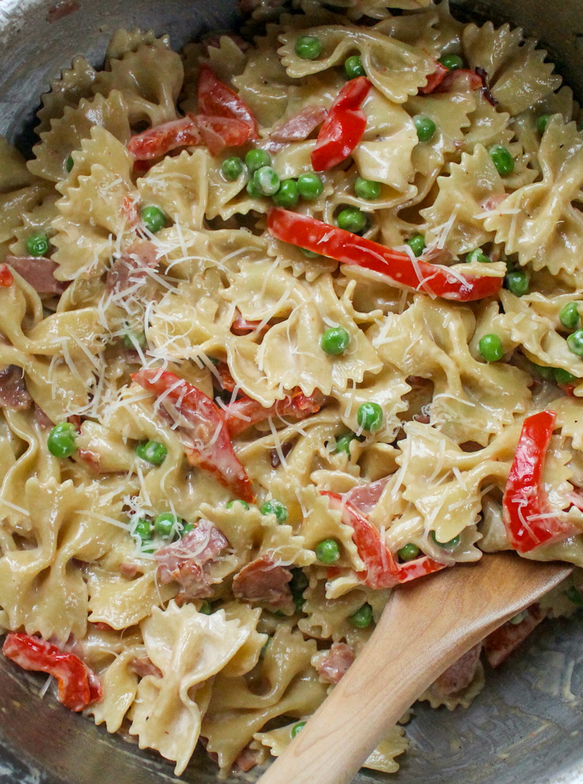 Creamy Farfalle Pasta with Prosciutto and Peas with a wooden spoon.