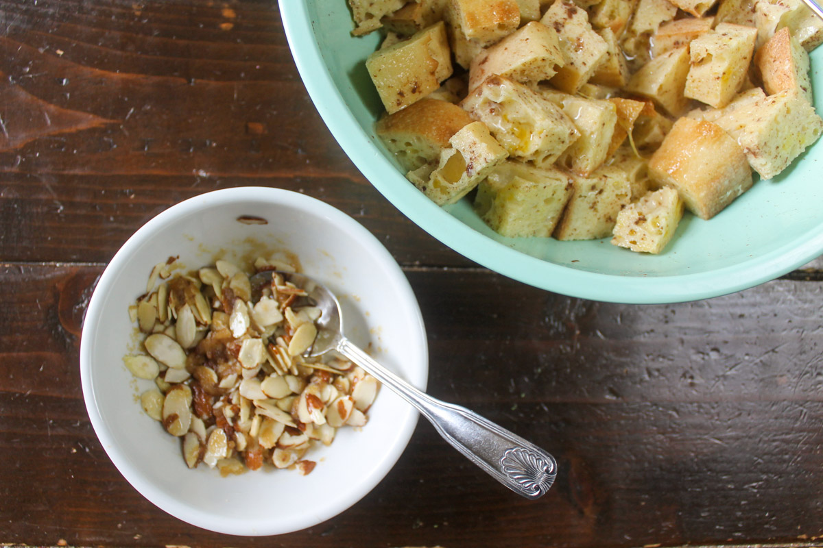 A small bowl of the almond topping next to a large bowl of the bread cubes soaking in the egg mixture.