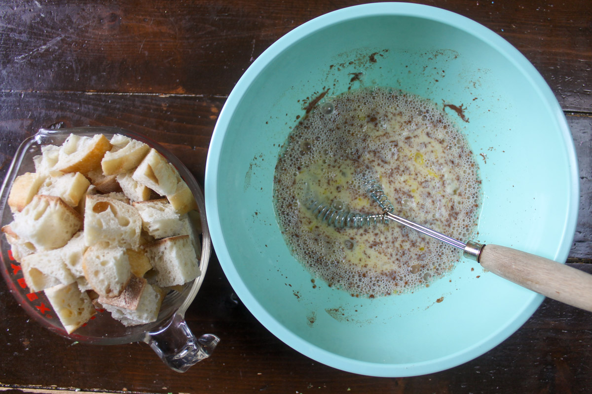 A bowl of egg cinnamon mixture whisked together and a glass measuring cup of cubed bread.