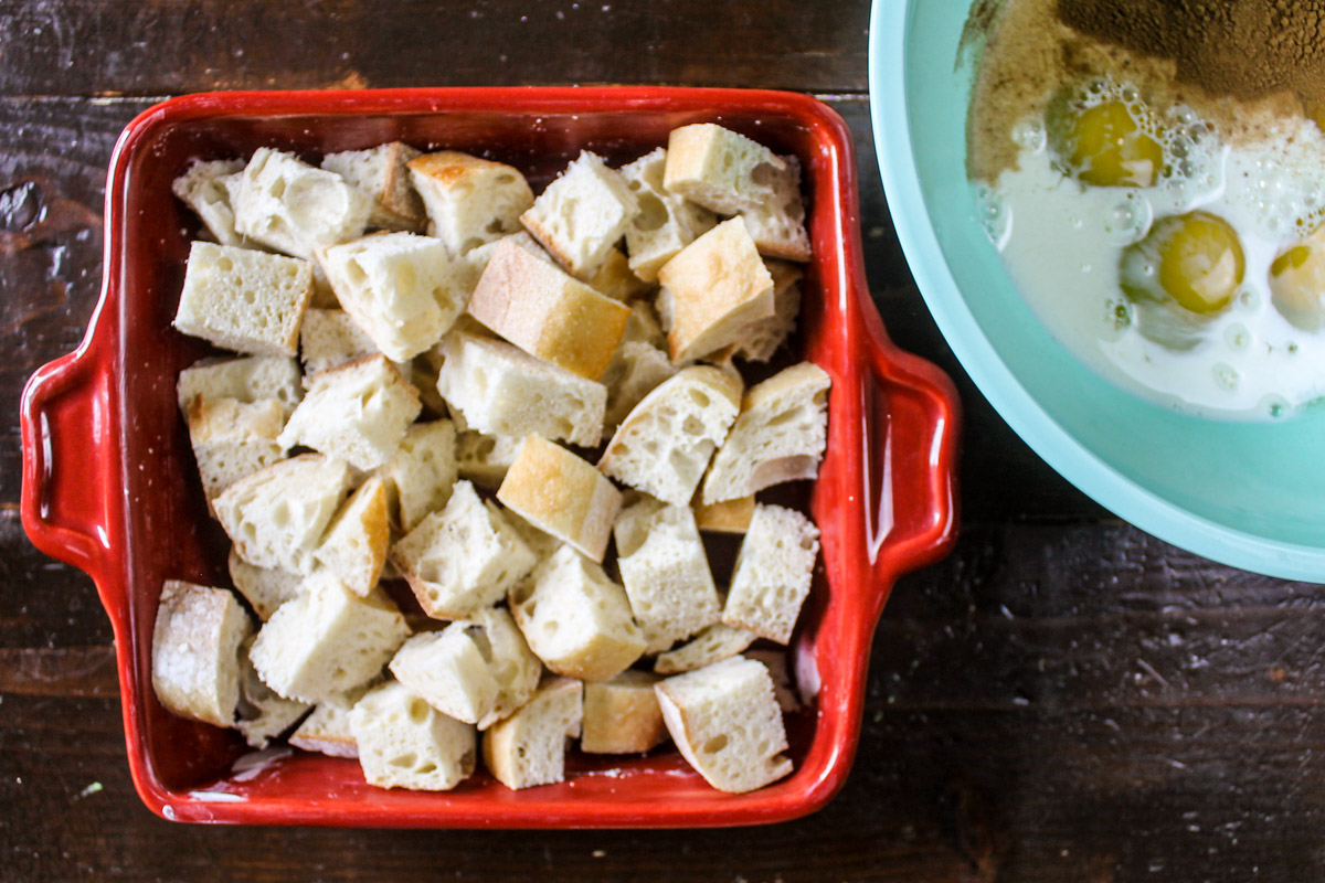 Filling a casserole pan with cubed bread and a bowl of egg and milk mixture for French toast casserole.