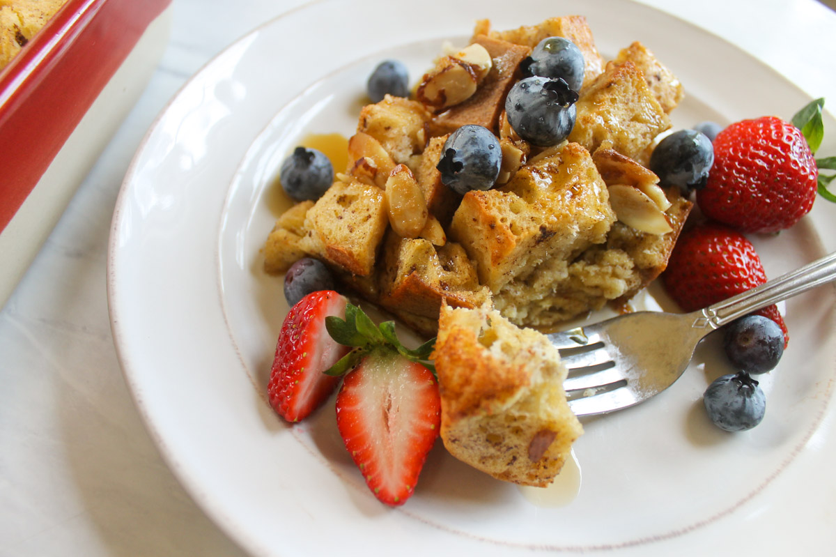 A serving of the baked French Toast Casserole on a white plate with blueberries and strawberries.