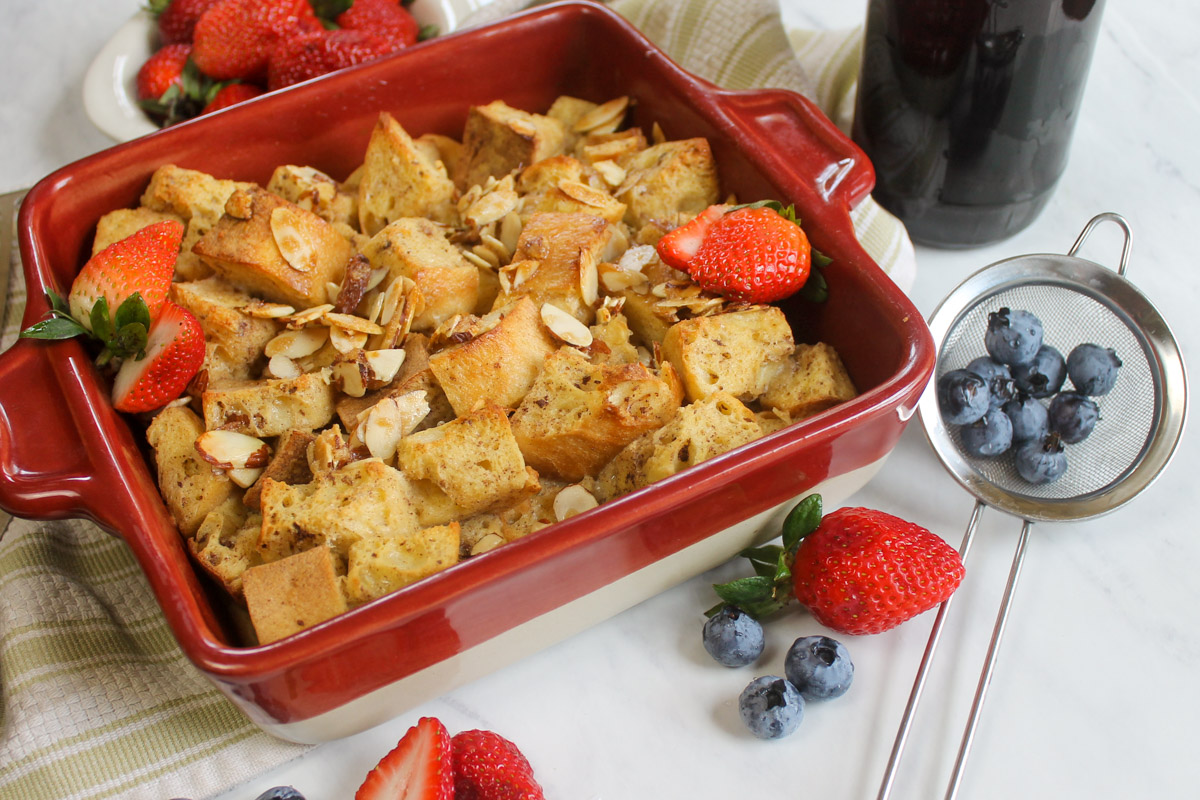 Baked French Toast Casserole with maple syrup and a strainer of blueberries.
