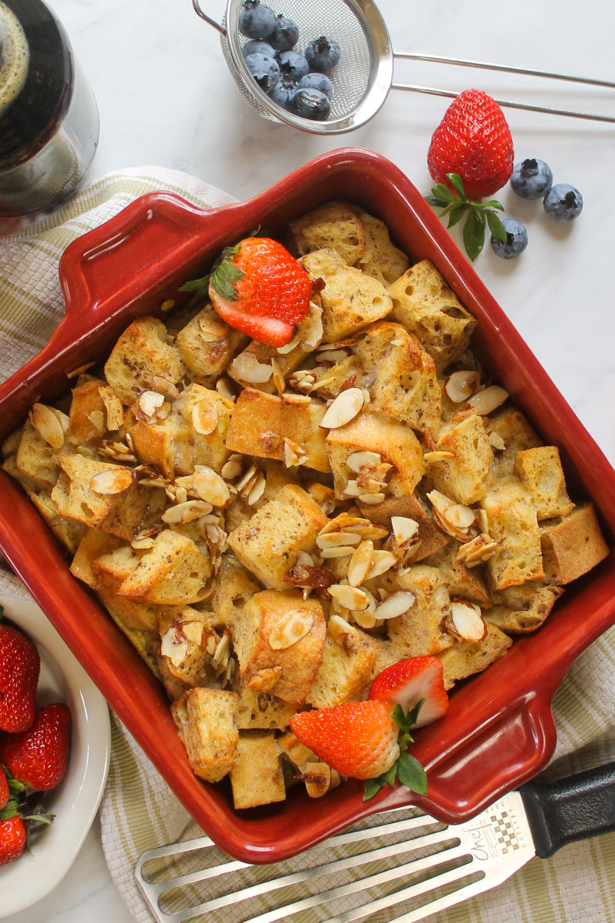 A French Toast Bake Casserole in a a red square pan with strawberries and blueberries.