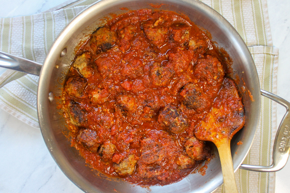 Meatballs simmering in marinara sauce with a wooden spoon.