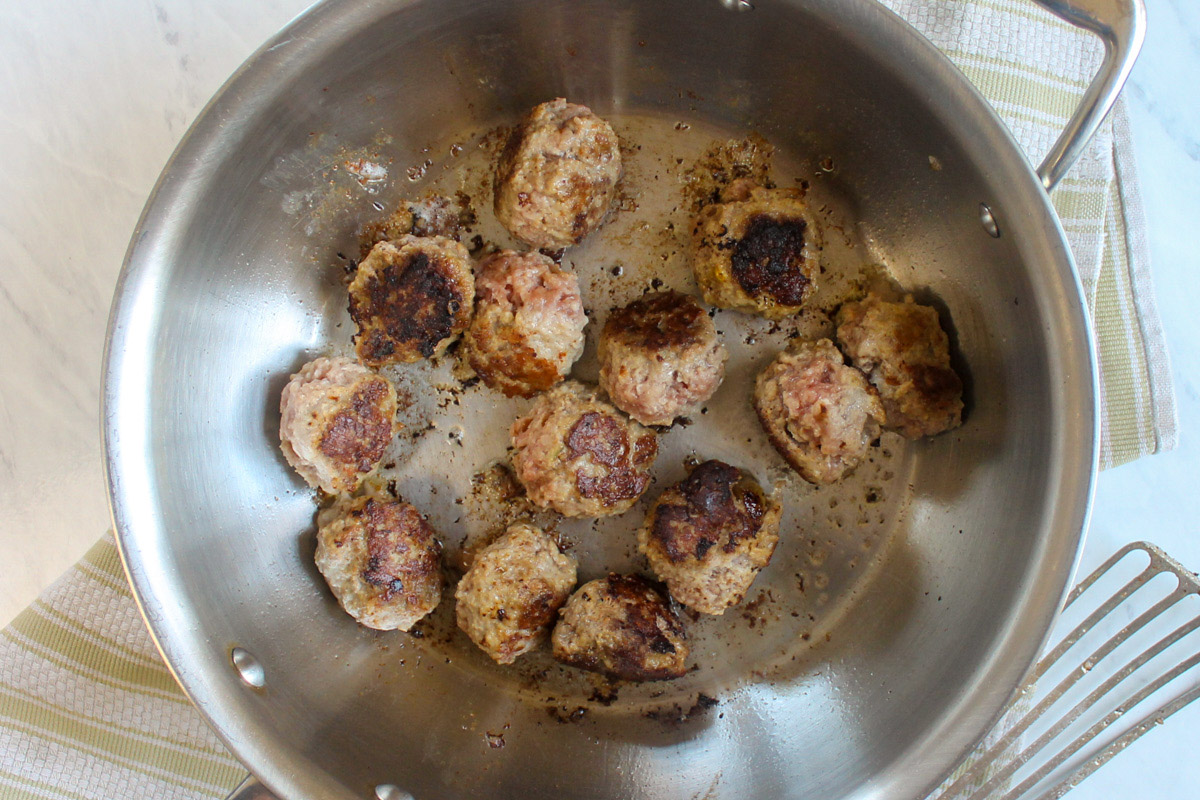 Meatballs being searing in a pan.