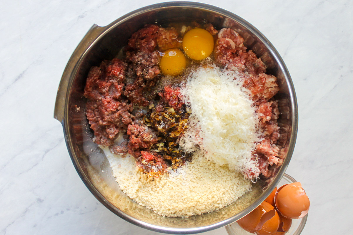 Meatballs ingredients in a bowl ready to be mixed next to a small bowl of egg shells.