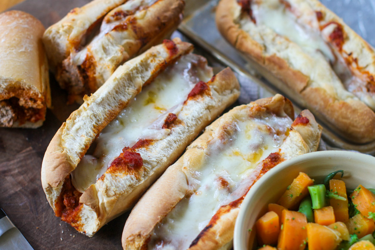 Meatball subs on a cutting board with a side bowl of vegetables.