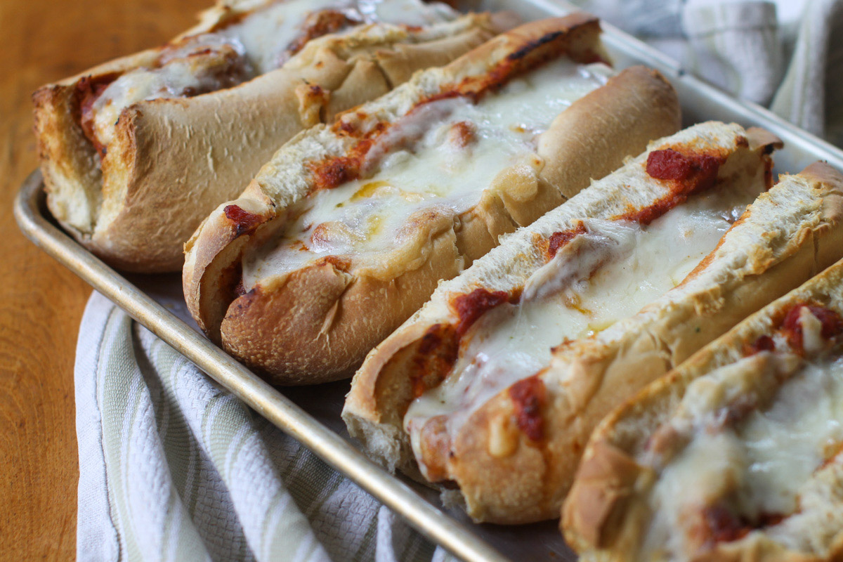 Meatball subs with melty white cheese on a sheet pan.