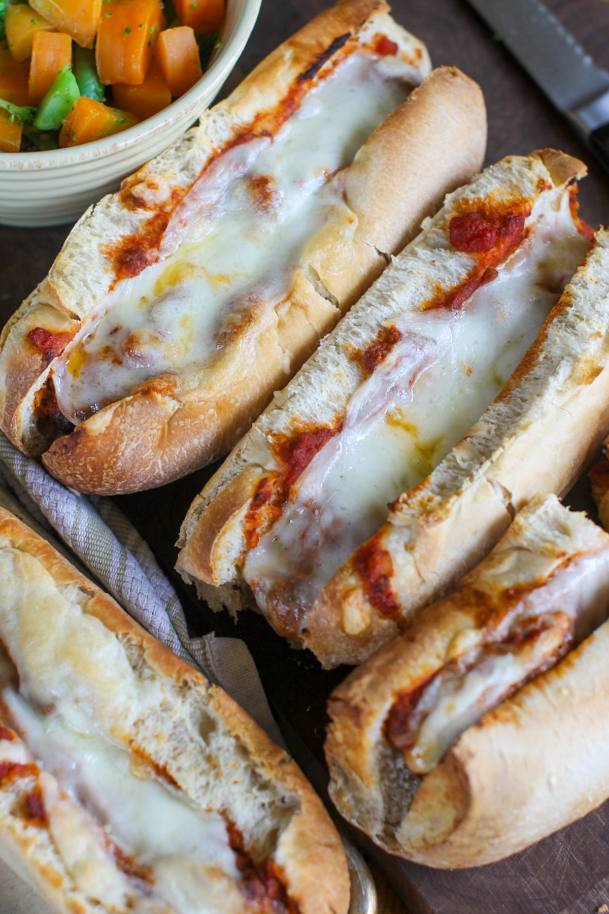 Meatball subs in marinara sauce with melty cheese on a cutting board.