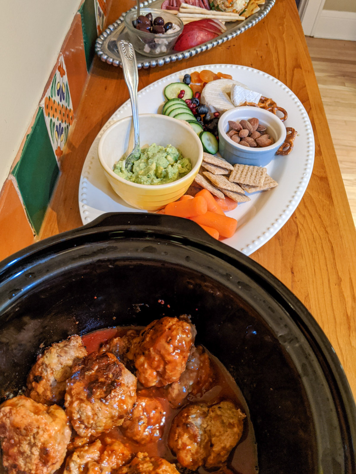 A crockpot of Sweet and Sticky Party Meatballs on a counter with other platters of appetizers.