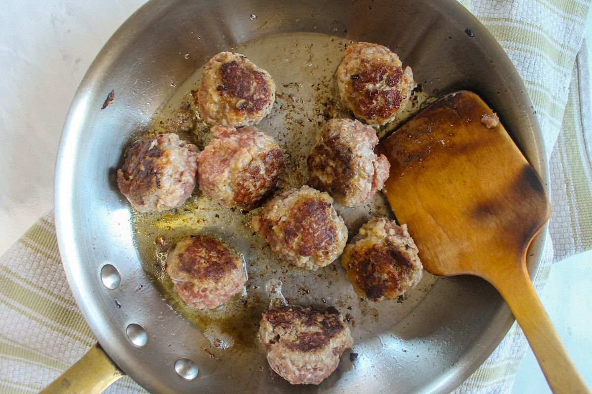 Searing meatballs in a skillet with a wooden spoon.