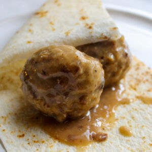 Two Norwegian meatballs in brown gravy wrapped in lefse.