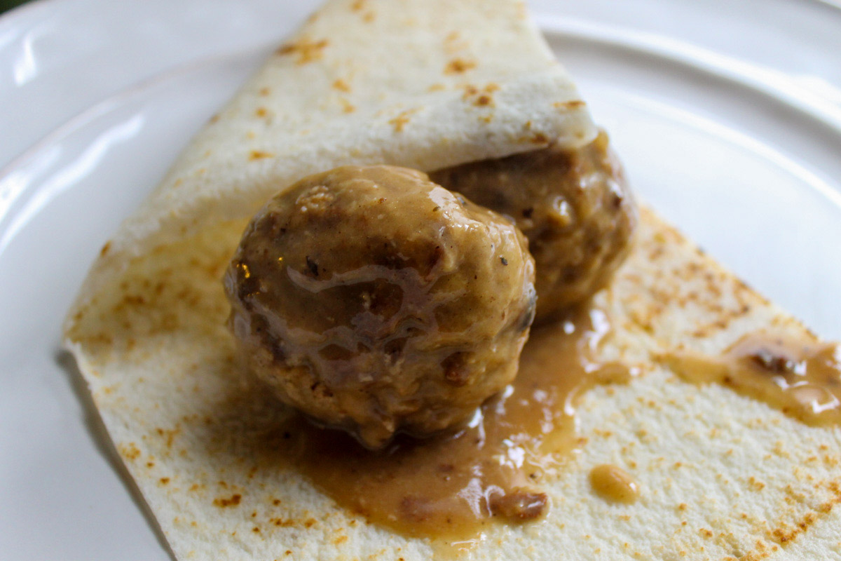 Norwegian Meatballs in brown gravy wrapped in lefse on a white plate.