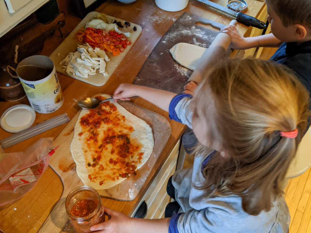 Kids making homemade pizza, adding pizza sauce
