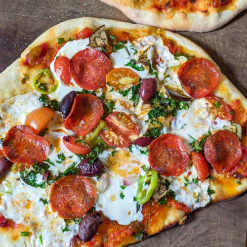 Homemade pizza on a cutting board with pepperoni, cheese and veggies.