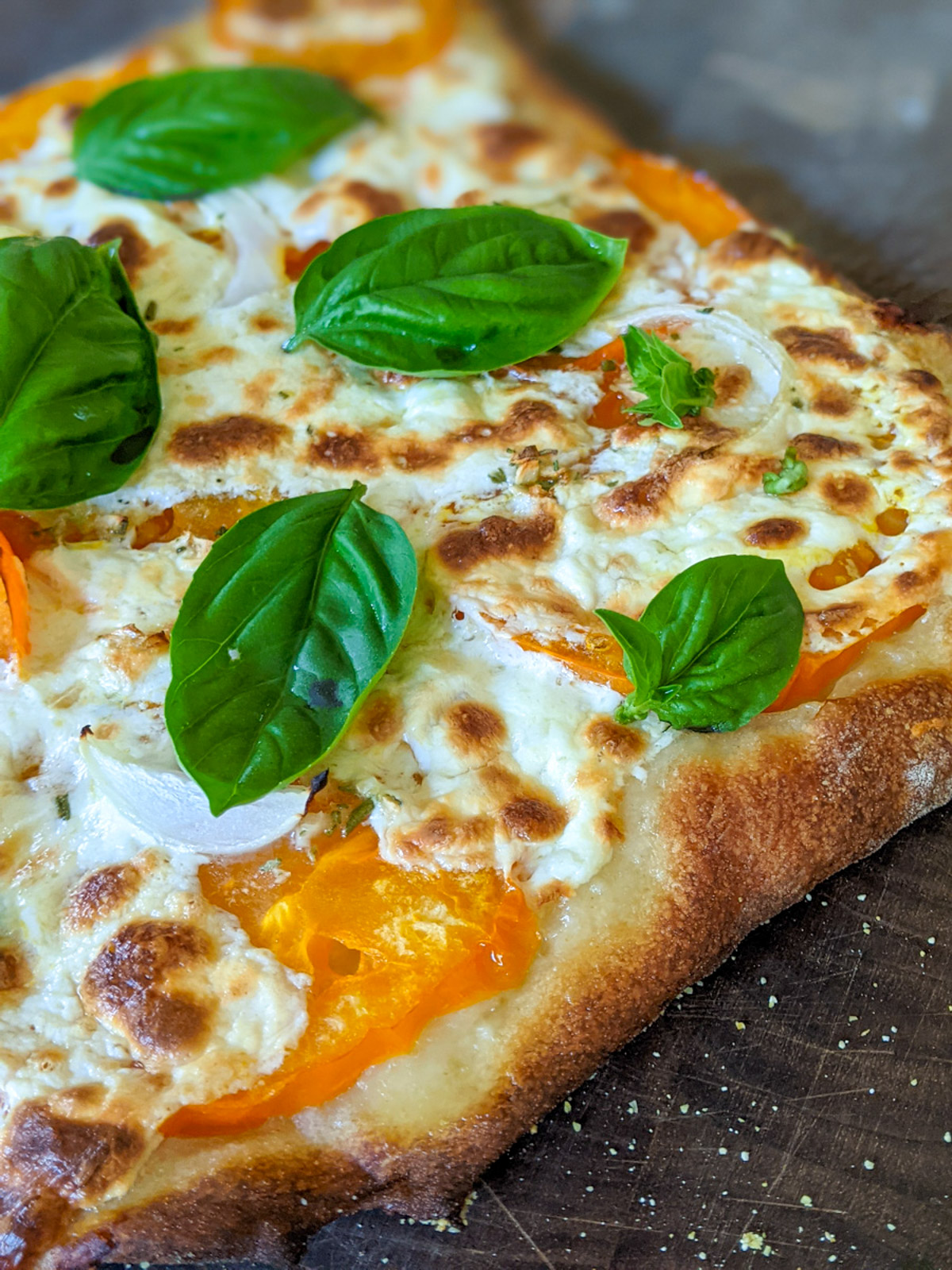 Homemade Pizza with yellow tomato slices, cheese and basil.