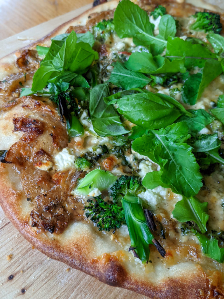 White pizza with broccoli, caramelized onion and arugula