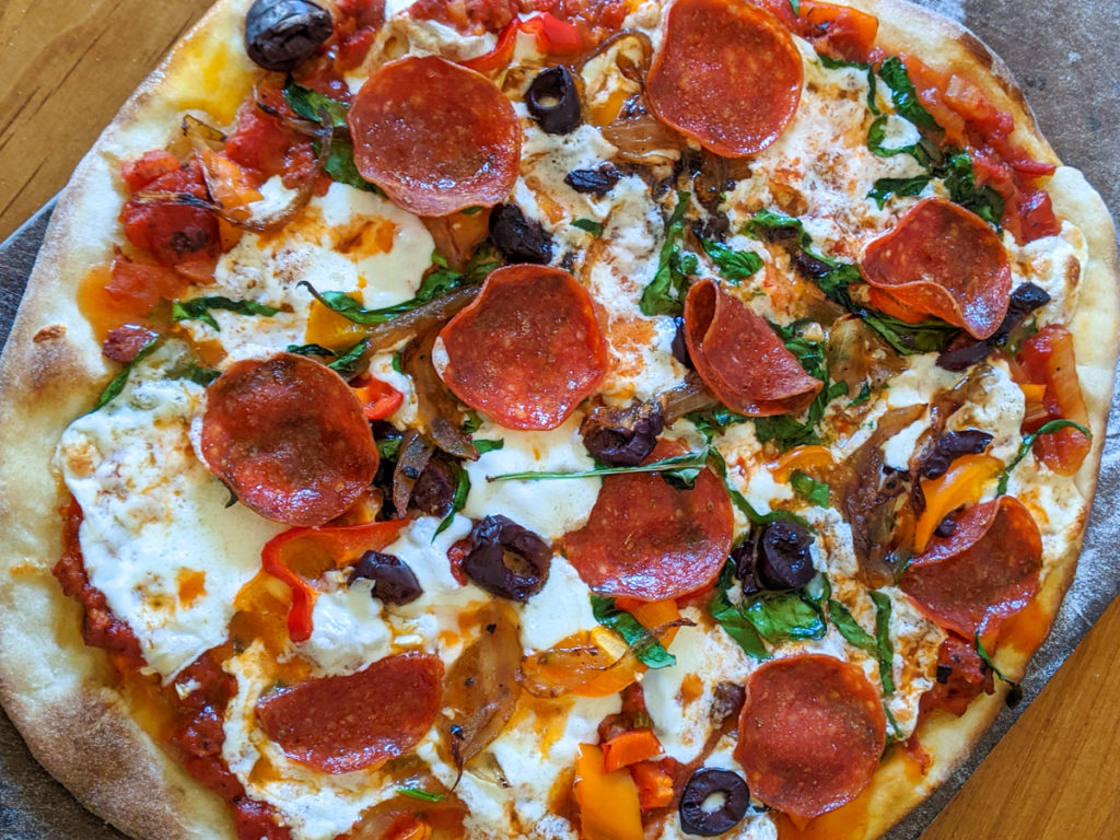 Homemade pizza with pepperoni, mozzarella, olives and fresh herbs