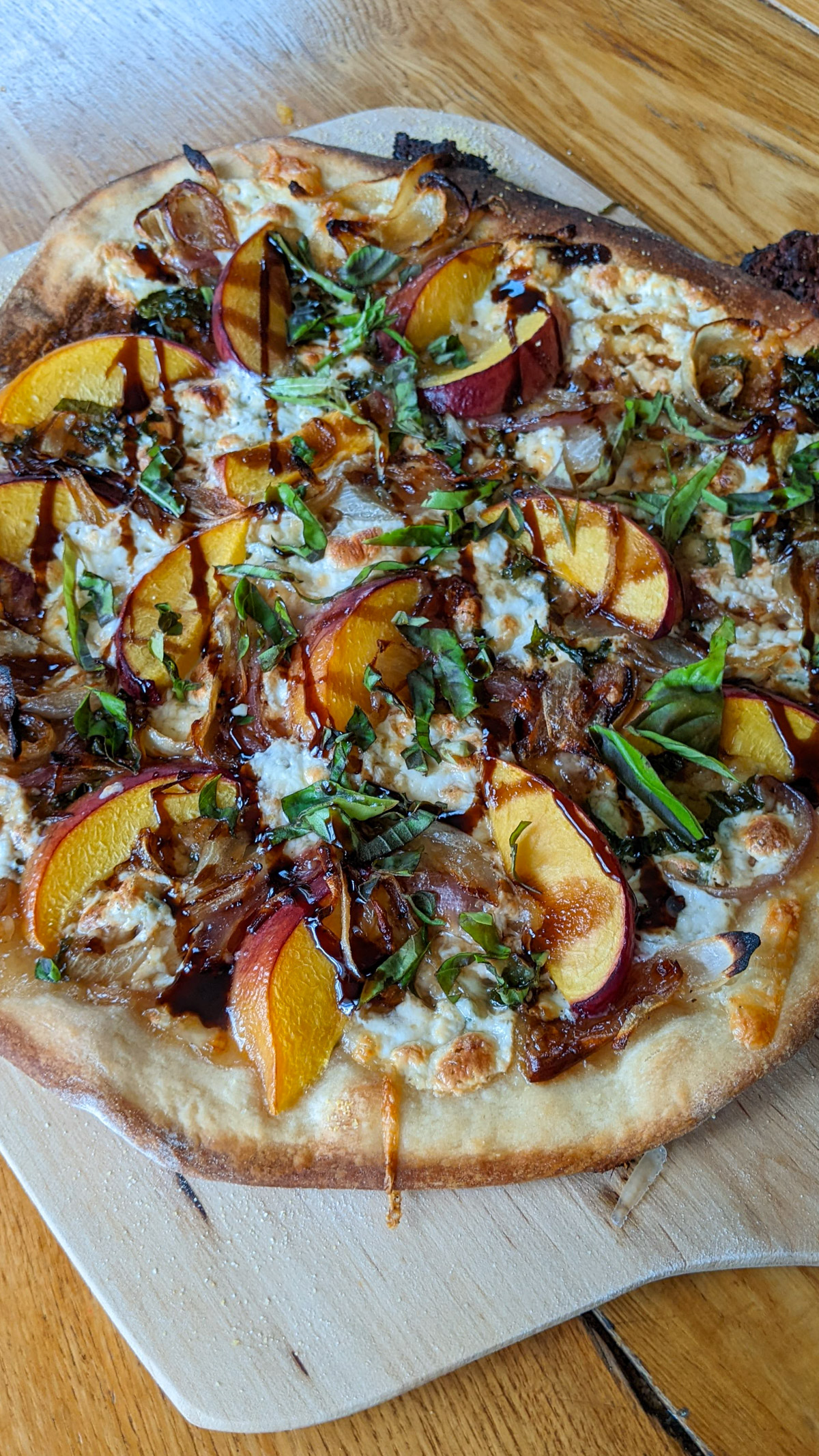 Peach pizza with caramelized onions, sliced peaches, arugula, cheese and balsamic glaze.