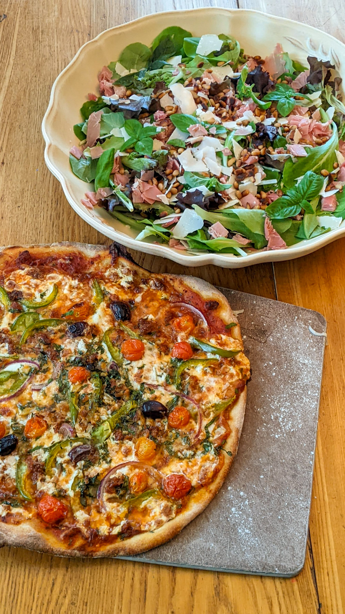A pizza next to a large salad with Parmesan and prosciutto.