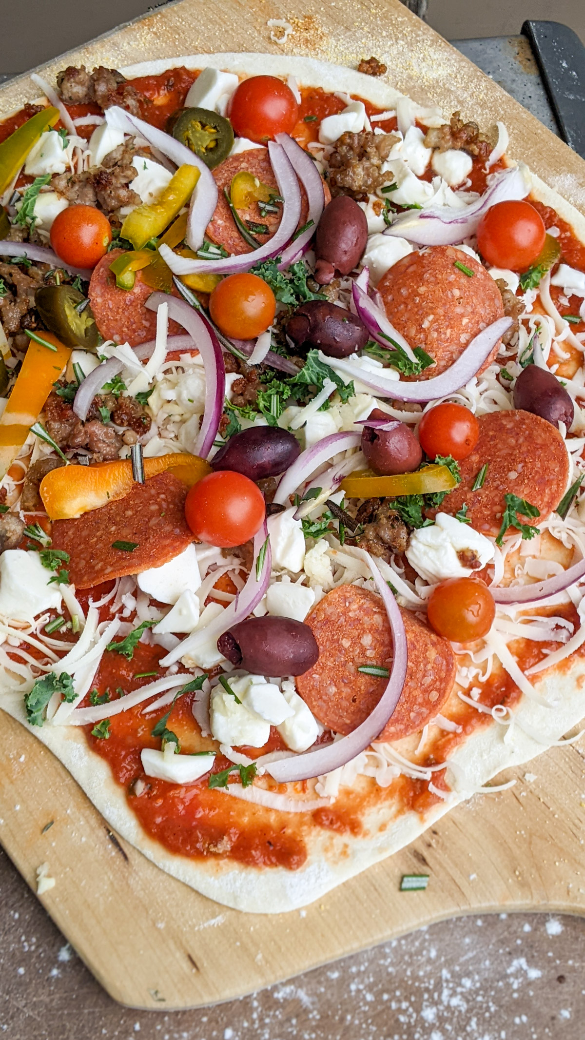 Making pizza with lots of toppings on a pizza peel ready to bake in the oven.