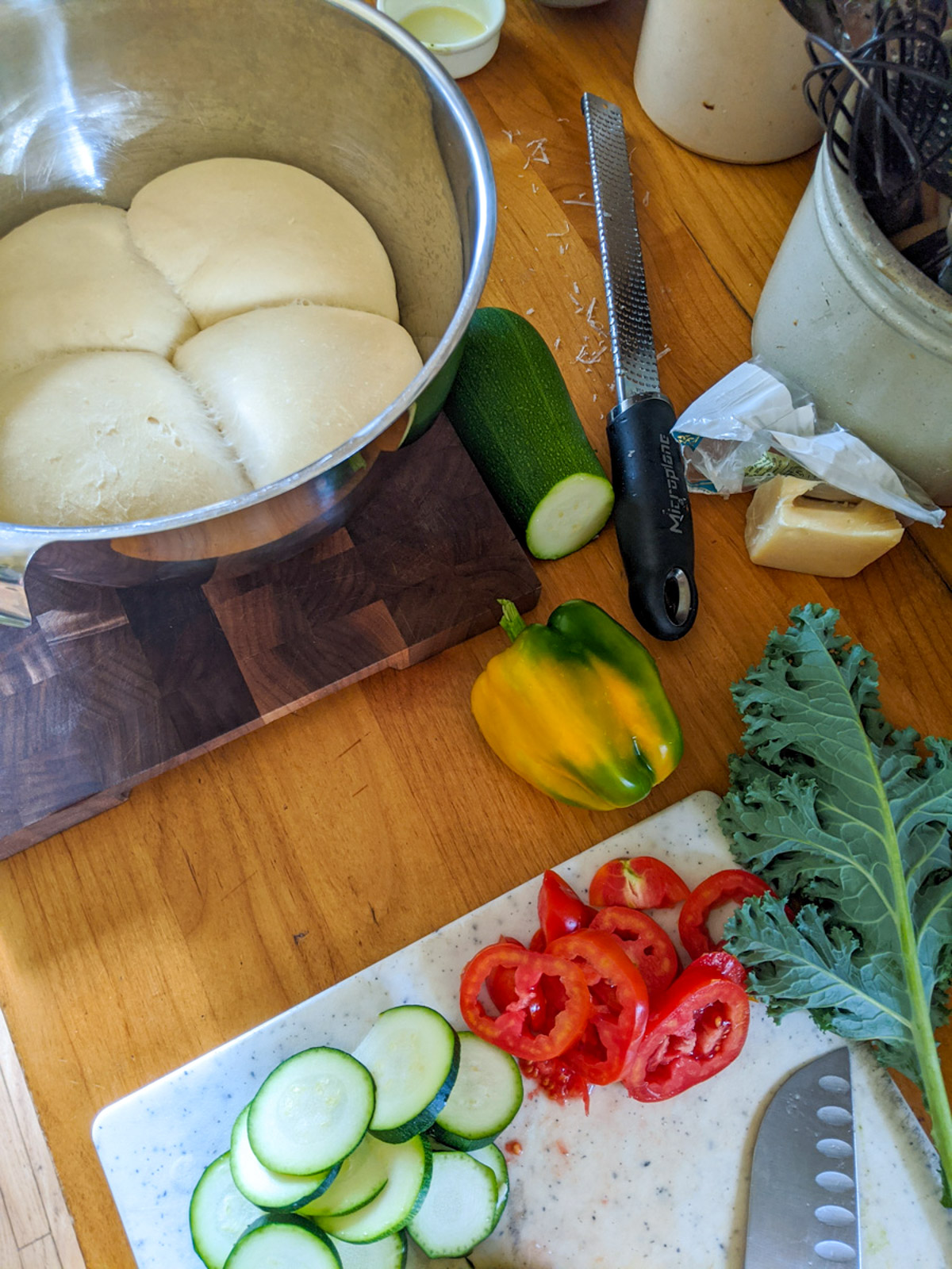 A bowl with four pizza dough balls and veggie toppings ready to make pizza. 