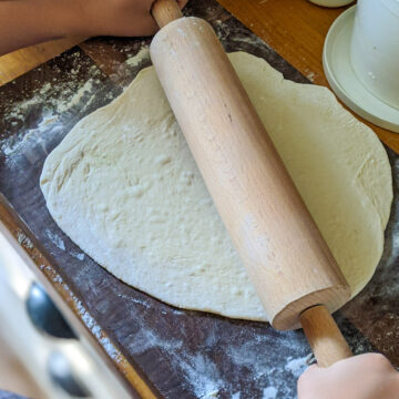 Rolling pizza dough with a rolling pin on a cutting board.