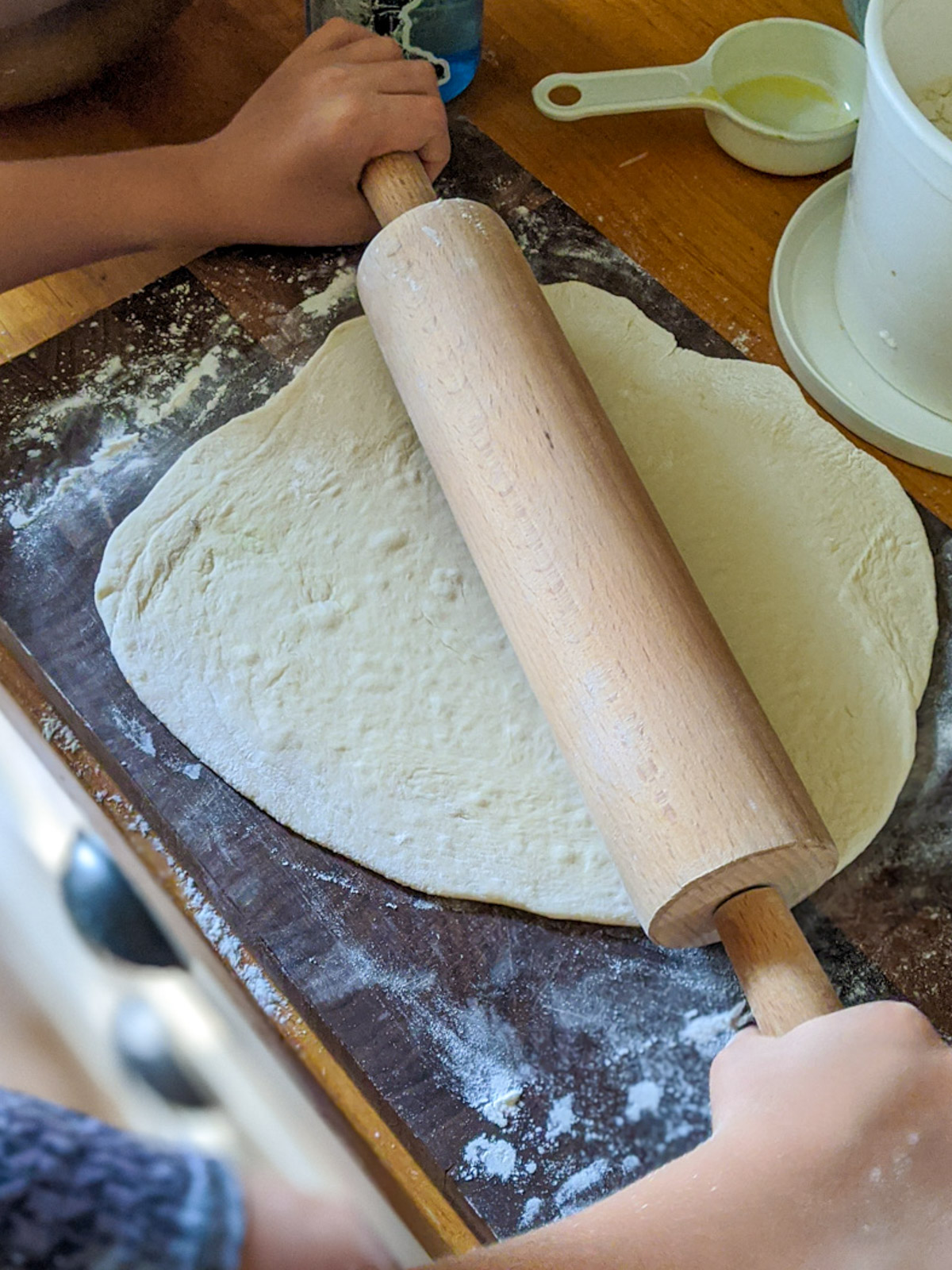 Rolling pizza dough with a rolling pin on a cutting board.