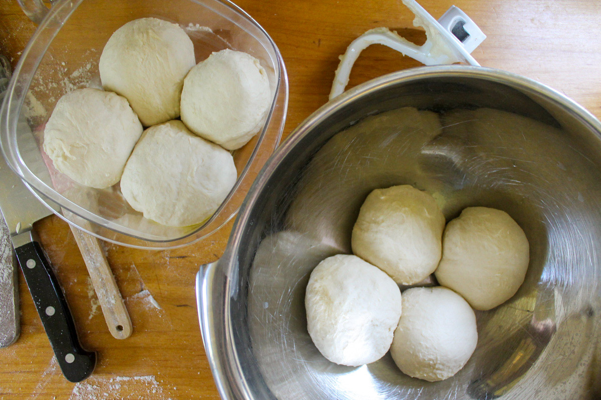 Homemade Pizza Dough balls portioned into a metal bowl and an extra container for the freezer.