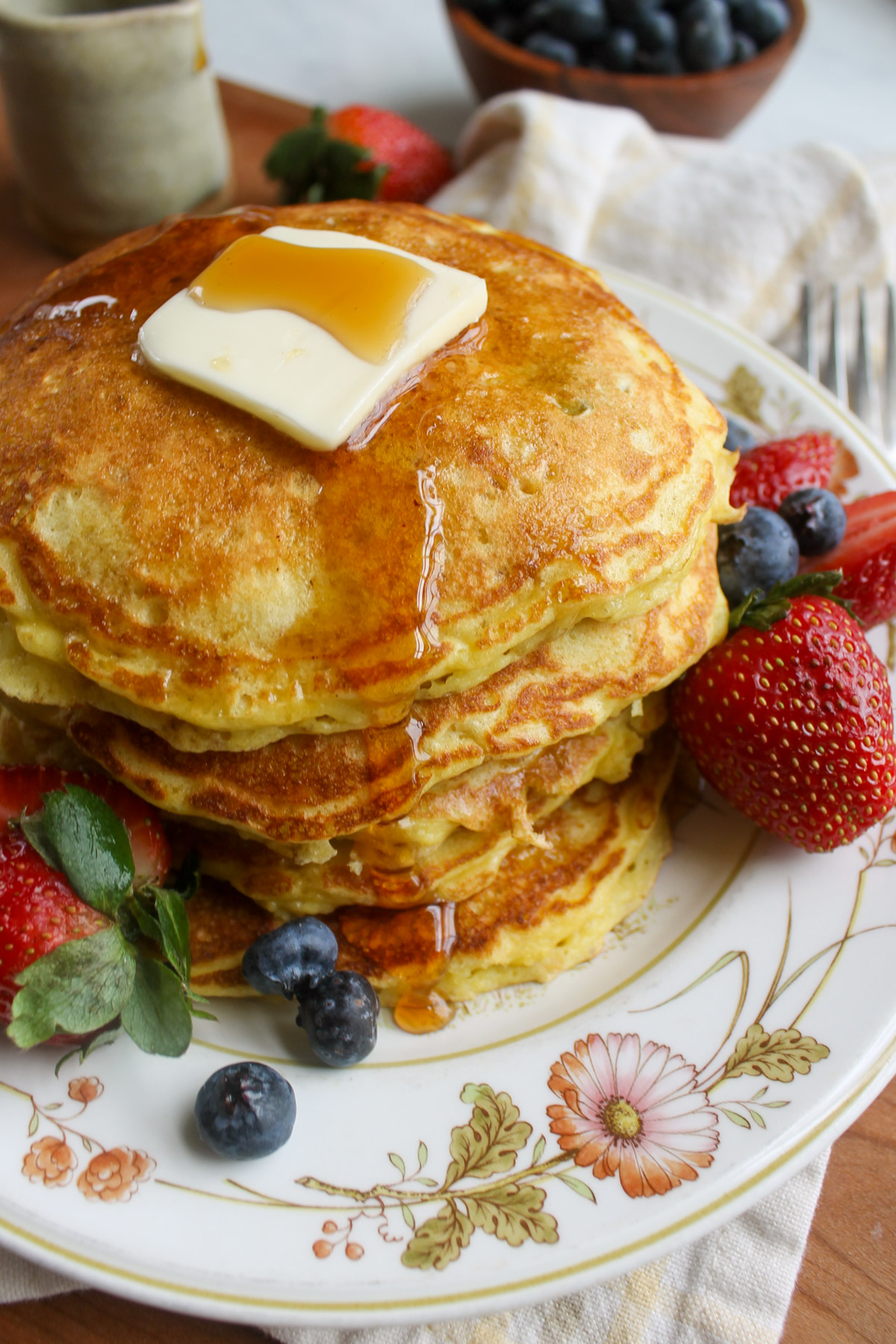 A stack of Protein Pancakes with butter and maple syrup with strawberries and blueberries.