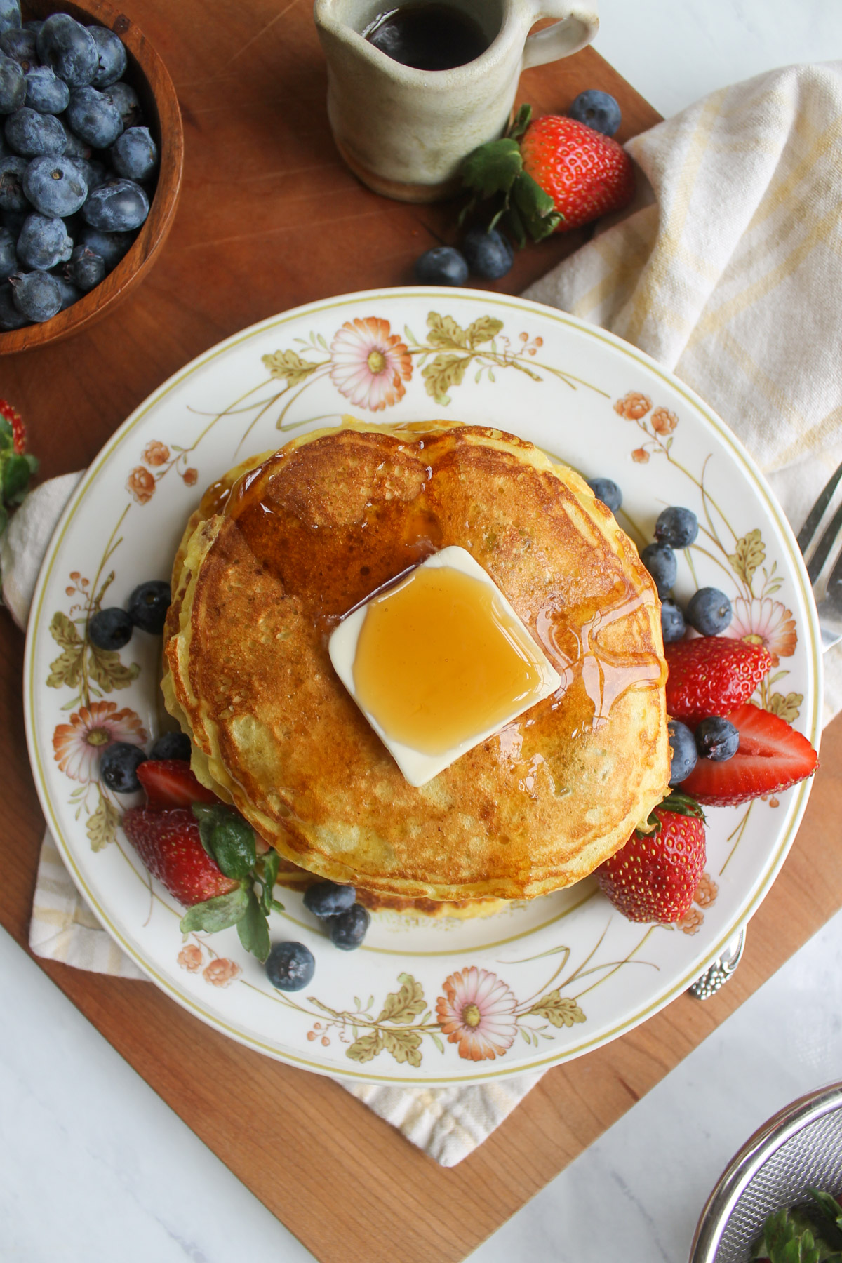 Pancakes on a flowered plate with butter, syrup and berries.