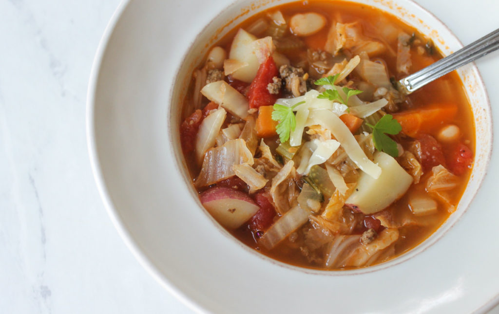 A white bowl of Beef Cabbage Soup with a spoon.